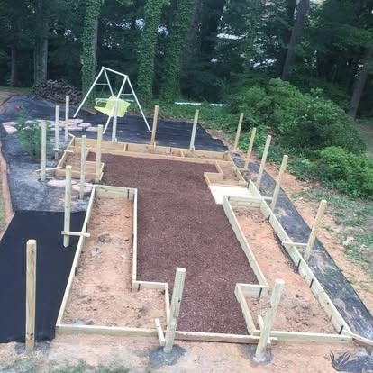 A backyard project showing wooden raised garden bed frames set on black landscape fabric with a swing set in the background.
