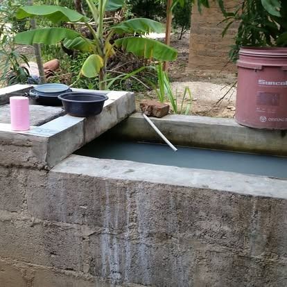 A stone structure containing a water basin, featuring a black bowl, a pink cylinder, and a brown bucket on the side.