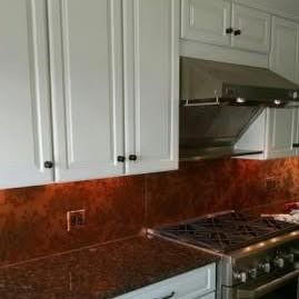 White cabinets above a copper backsplash and a granite countertop with a stainless steel range stove.