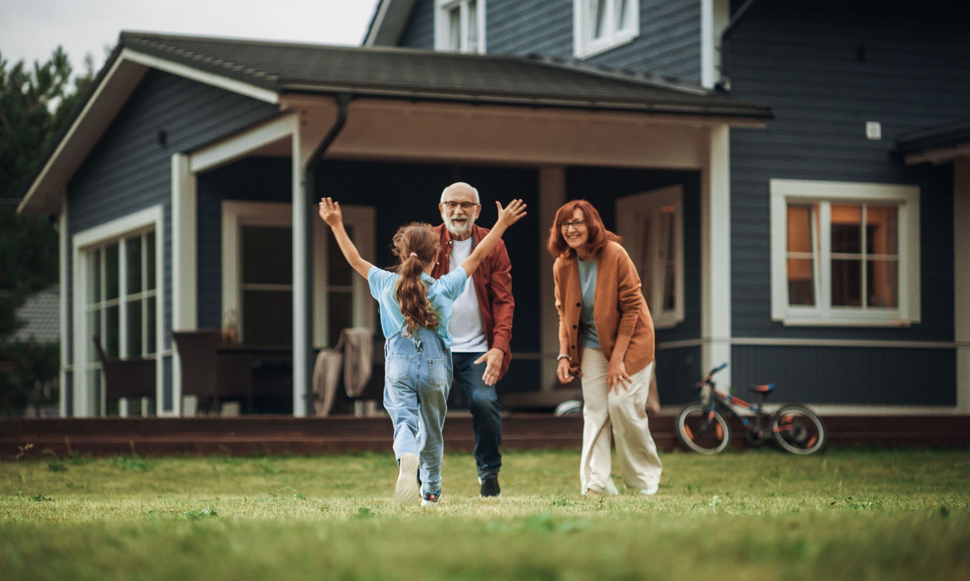 Girl running to embrace grandparents in front of a blue house; green lawn.