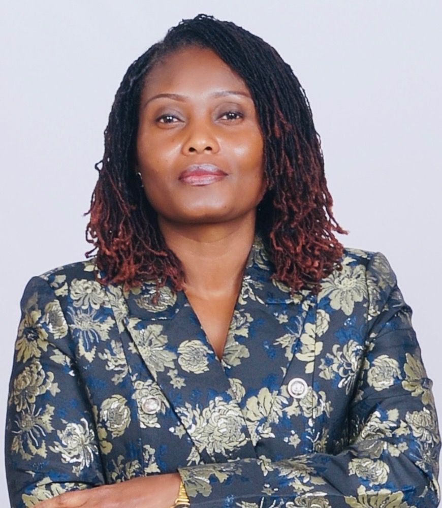 A woman is sitting at a desk with a laptop and a vase of flowers.