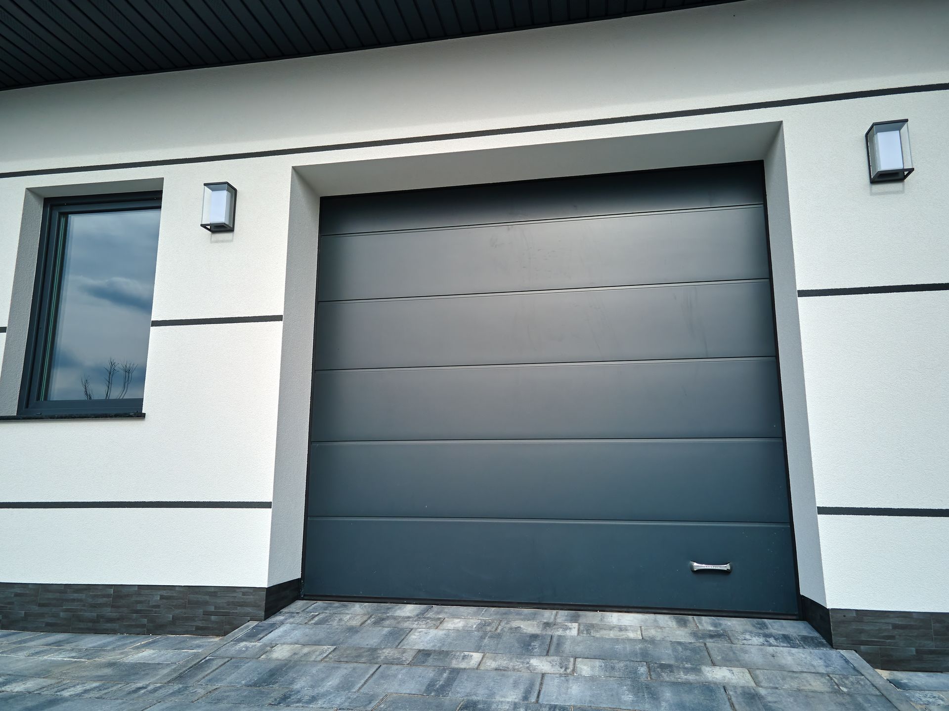 A black garage door is sitting in front of a white house.