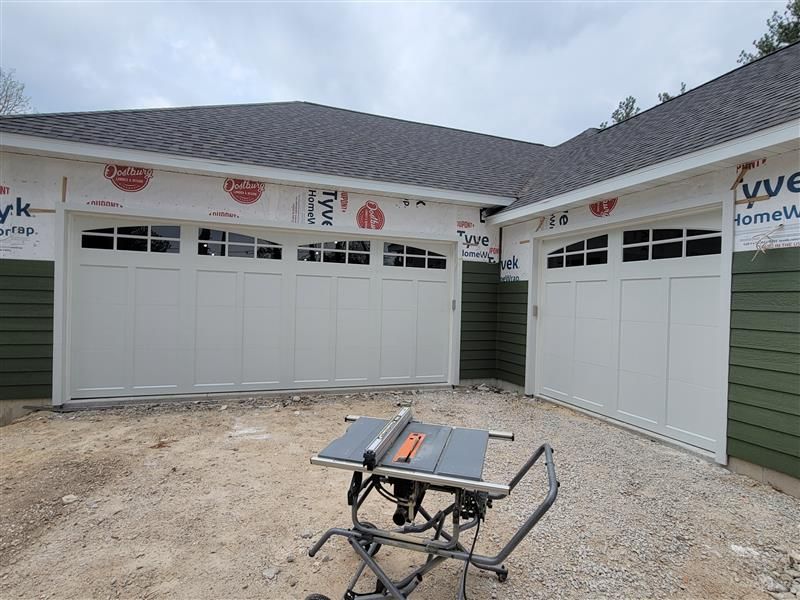 A large gray garage door is sitting in front of a brick house.