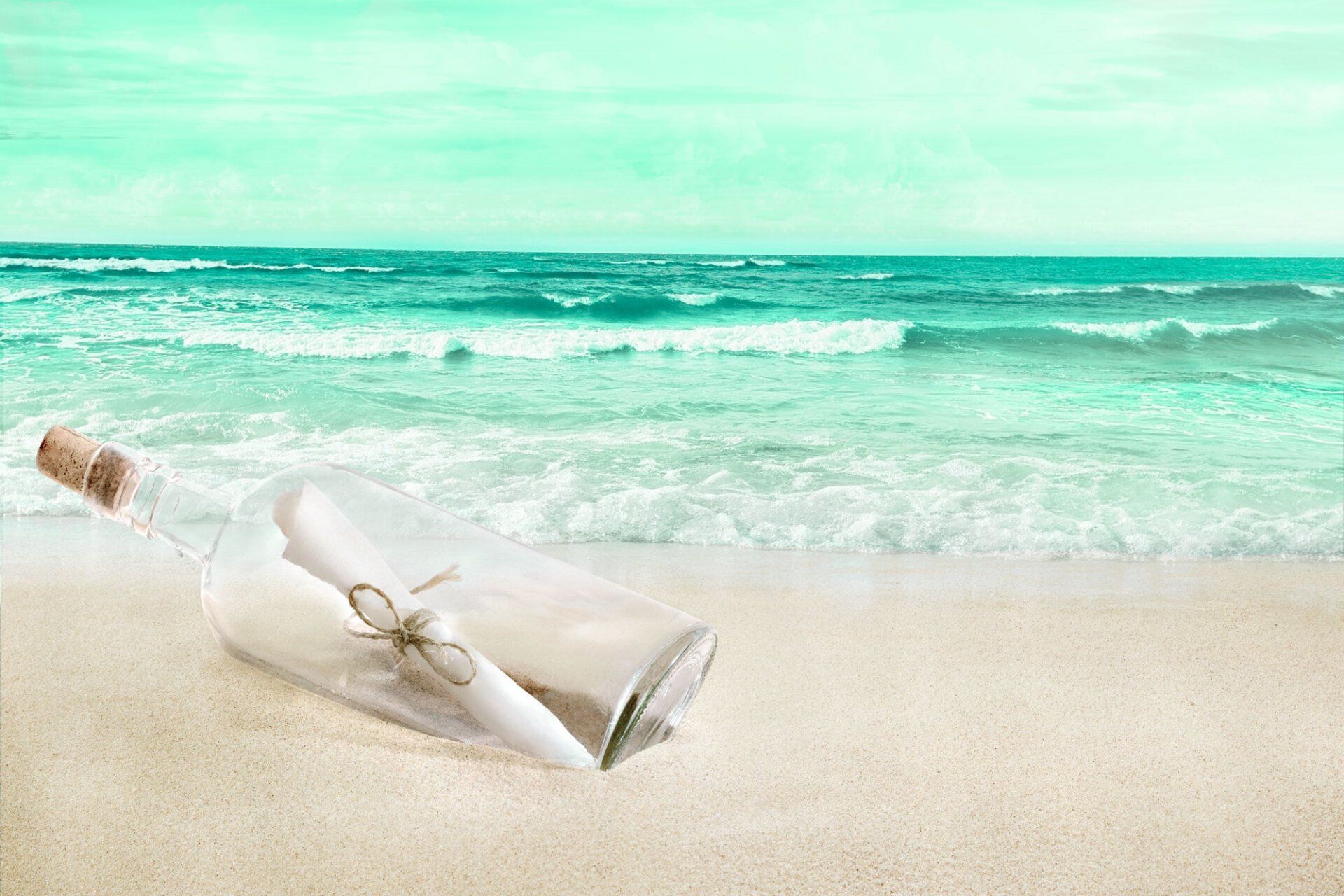 messaggio in una bottiglia di vetro chiusa con tappo di sughero, ancorata sulla spiaggia in riva ad un mare mosso sullo sfondo