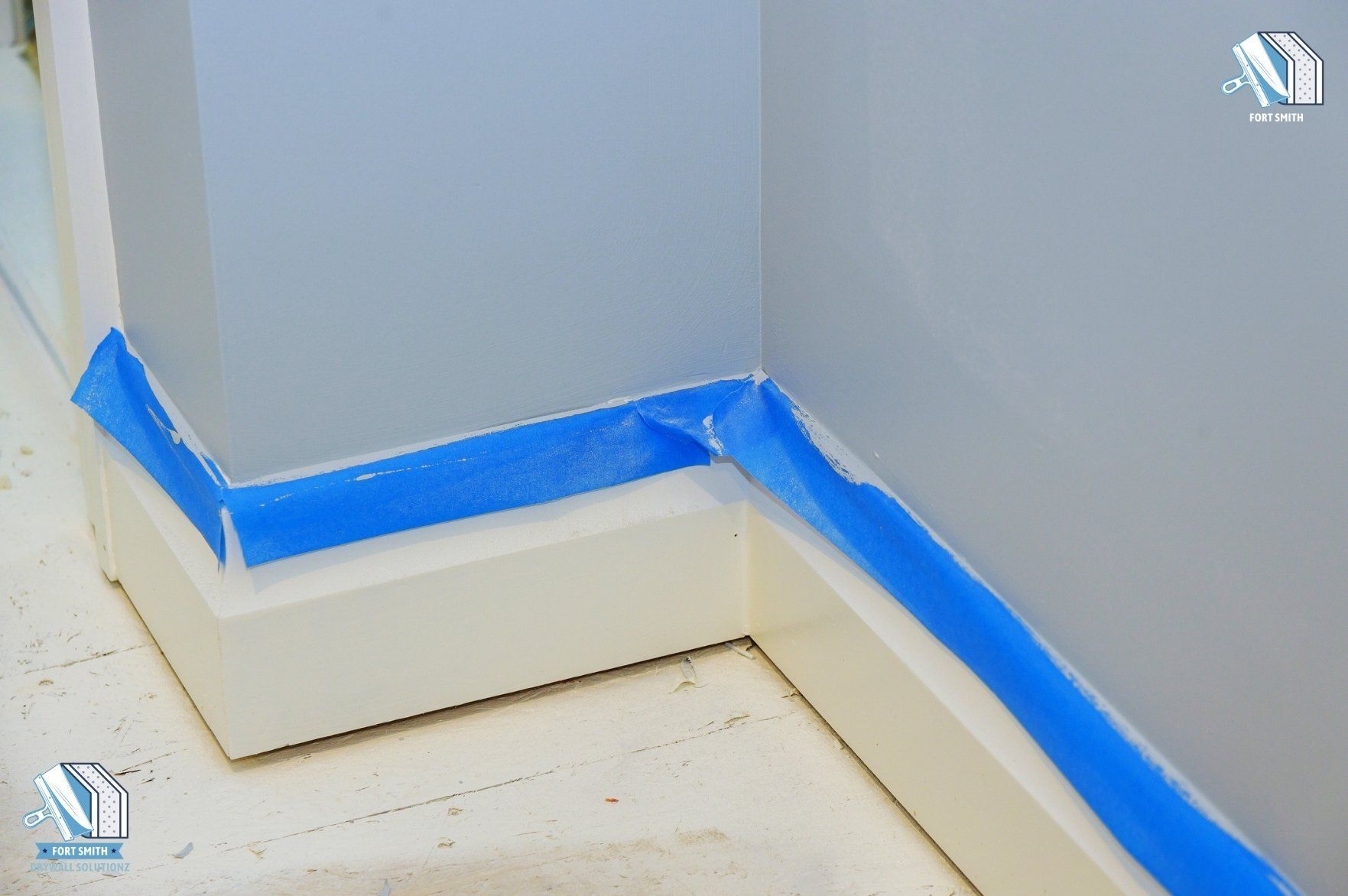 A blue painter’s tape is neatly arranged around the baseboards ready for a wall painting project. This indicates the final stages of drywall finishing, with preparation for interior painting. This image represents professional interior painting services in 10017 Foxboro Rd, Fort Smith, AR.