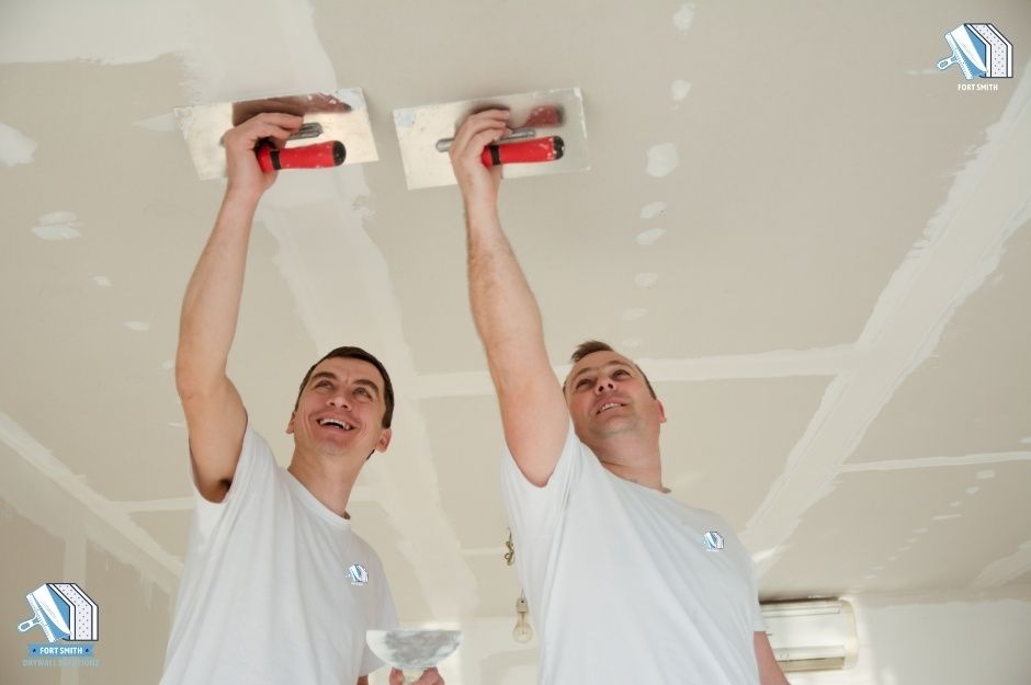 A close-up view of two contractors in their mid-40s skimming a ceiling with sheetrock mud. They are wearing white uniforms and carefully smoothing the surface to finish the drywall. The image highlights sheetrock mudding and taping services in 1005 S N St, Fort Smith, AR.