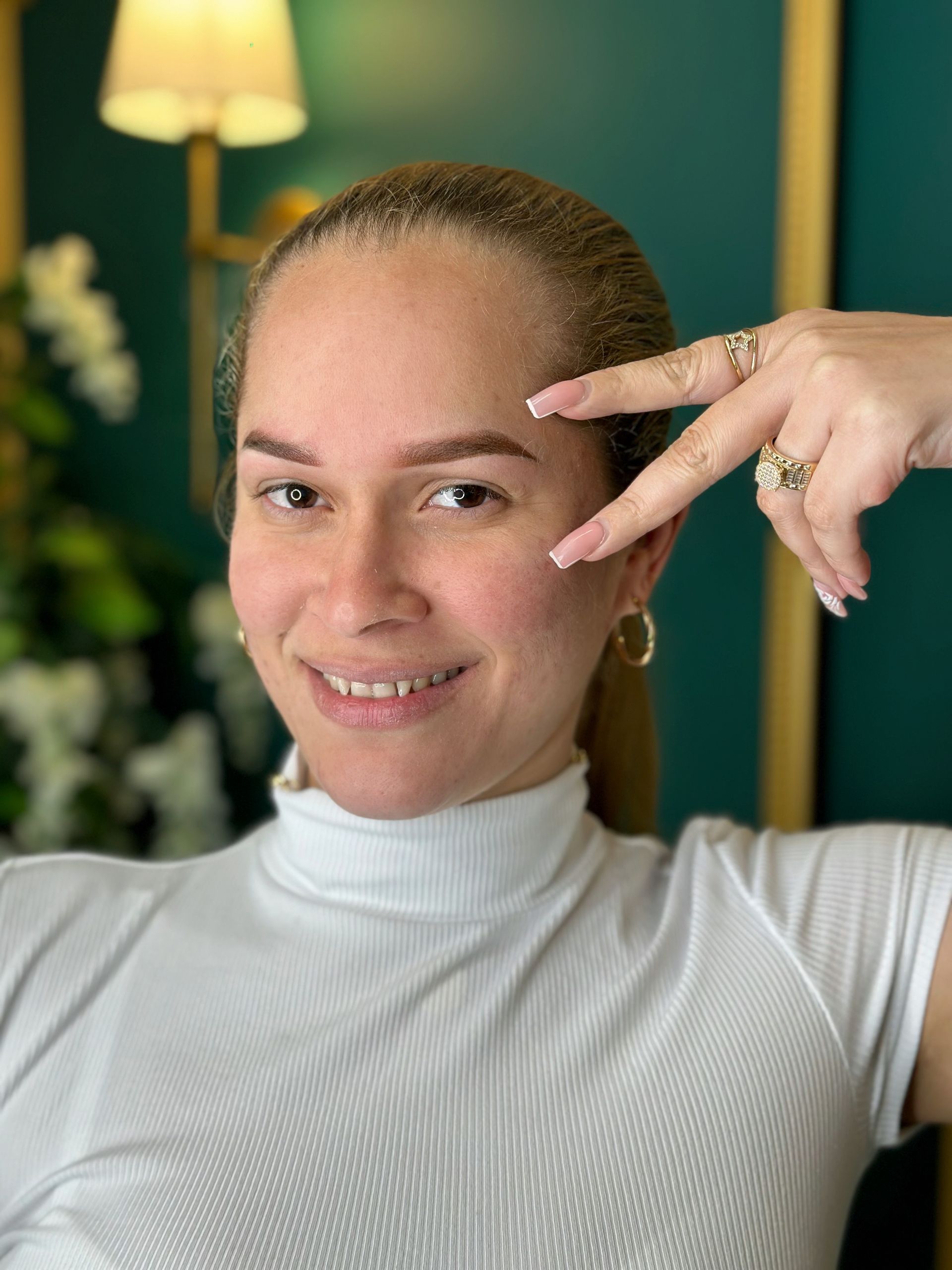 The woman is wearing a white turtleneck and a ring on her finger.
