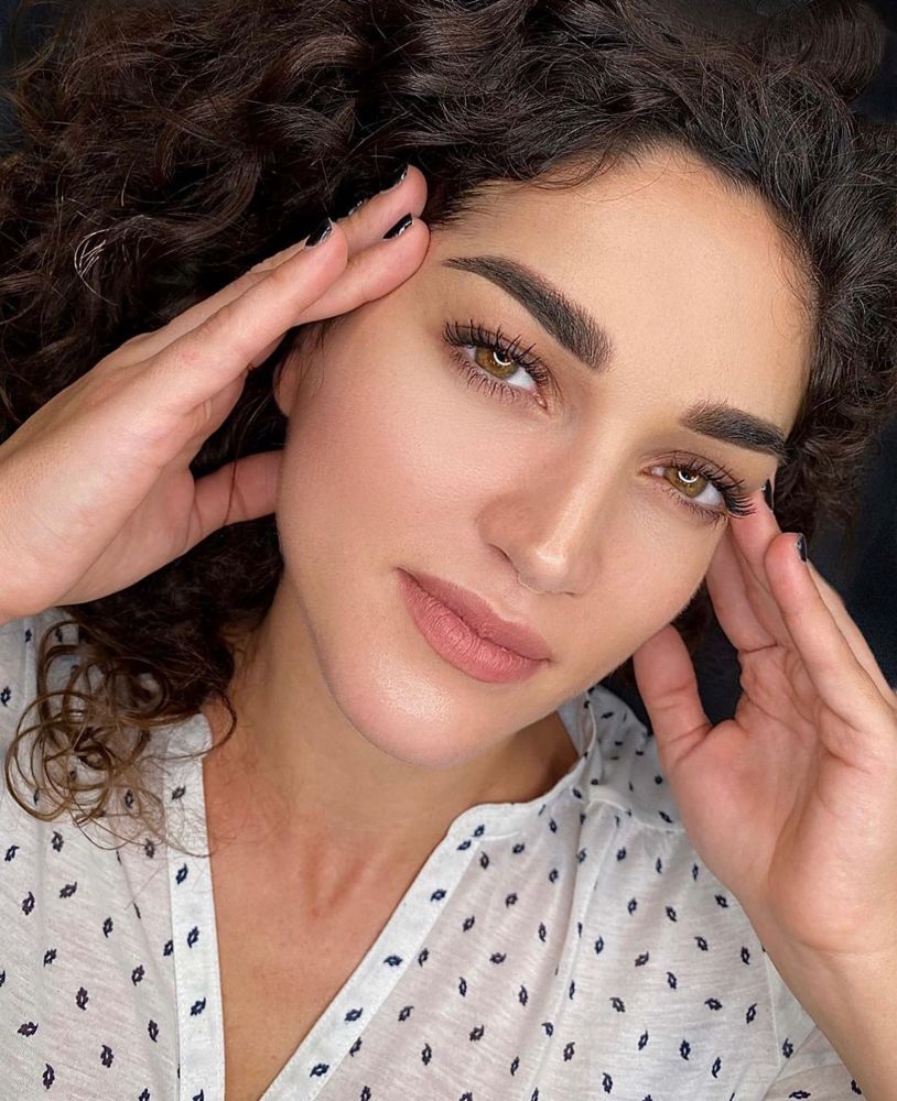 A woman with curly hair is touching her forehead with her hands