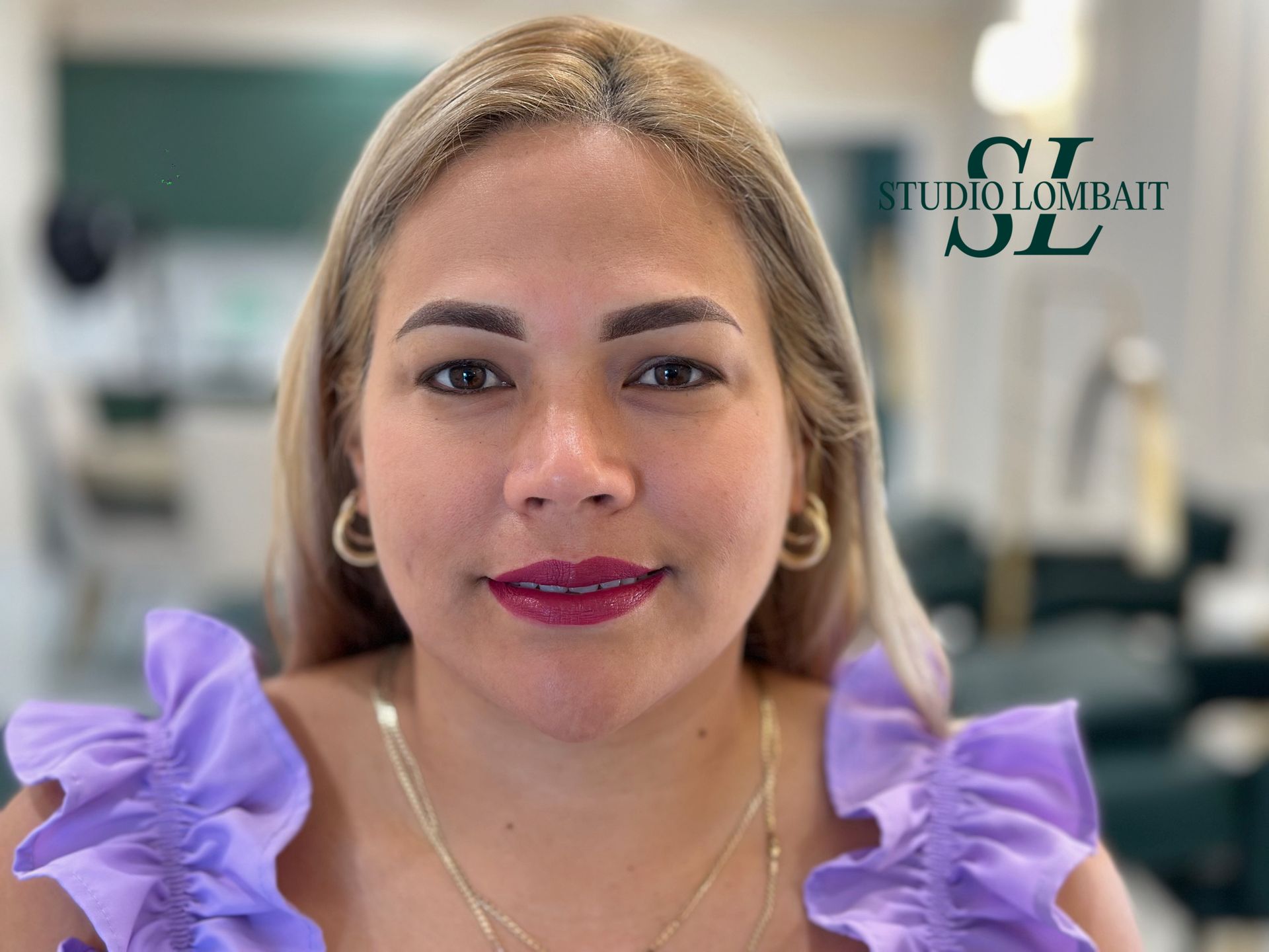 A woman wearing a purple top and earrings is looking at the camera.