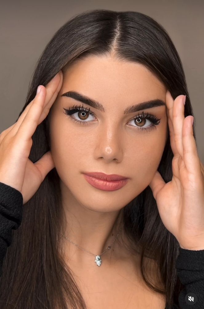 A close up of a woman 's face with her hands on her forehead.