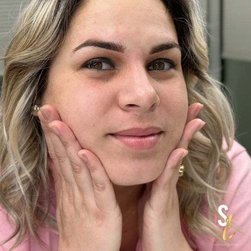 A woman in a pink shirt is holding her face with her hands.