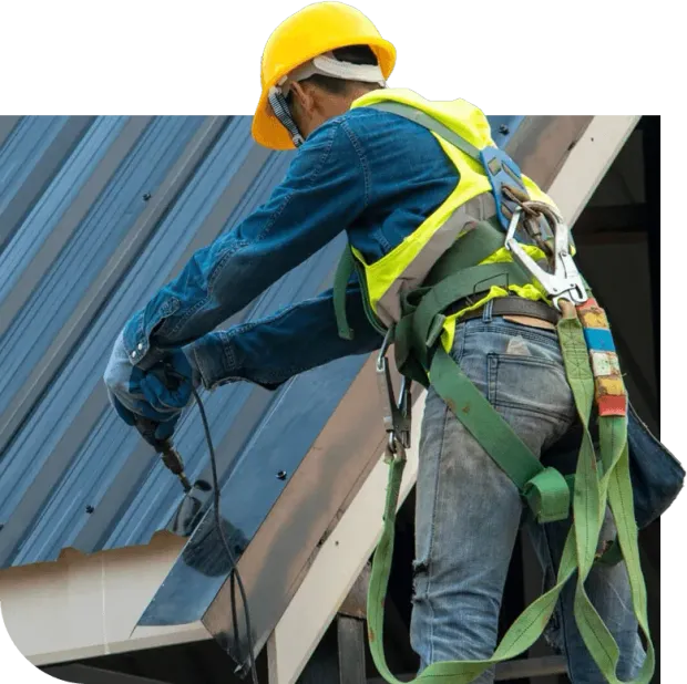 A man wearing a hard hat and safety harness is working on a roof.