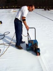 A man is working on a white roof with a machine.
