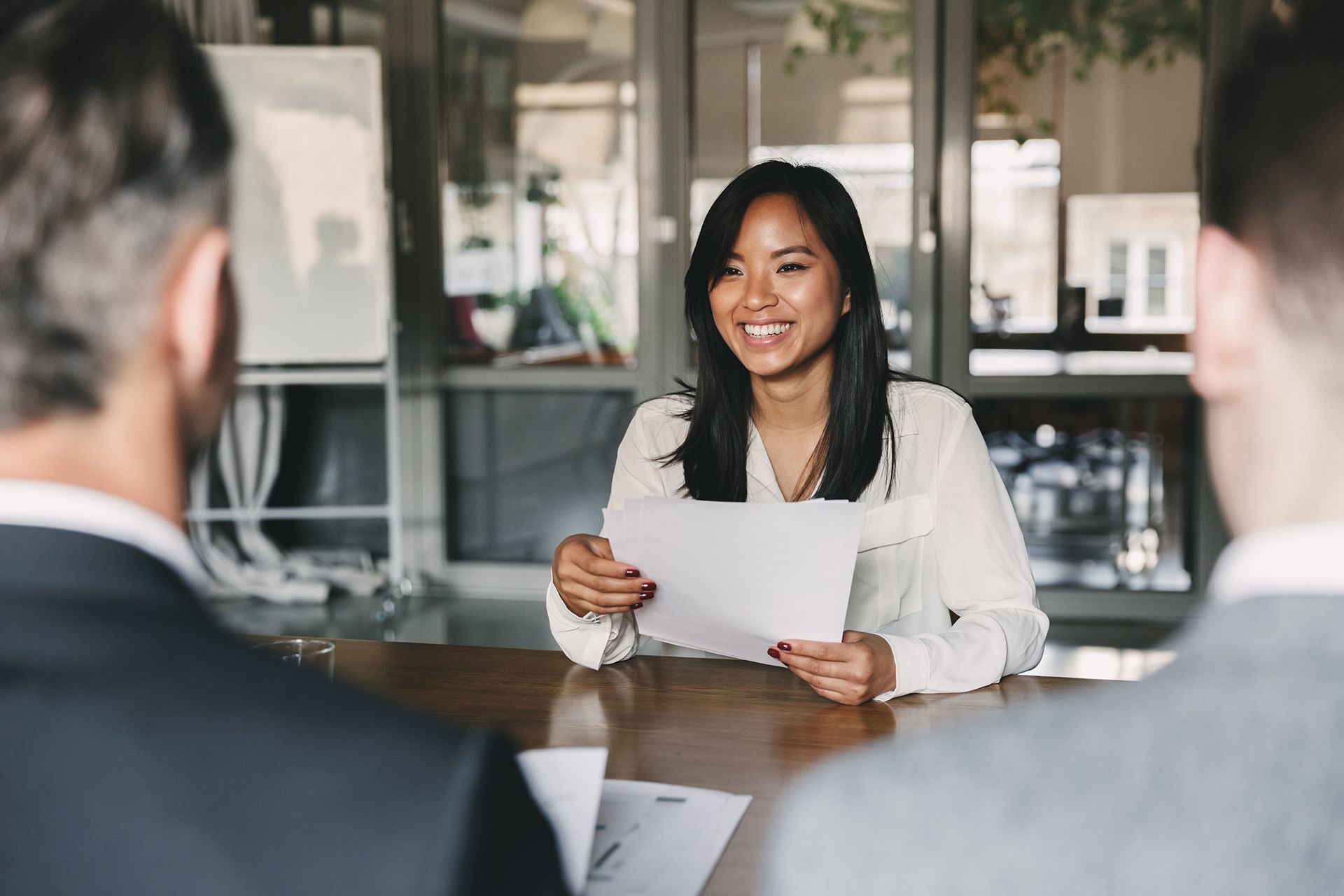 A woman is sitting at a table holding a piece of paper during a job interview.