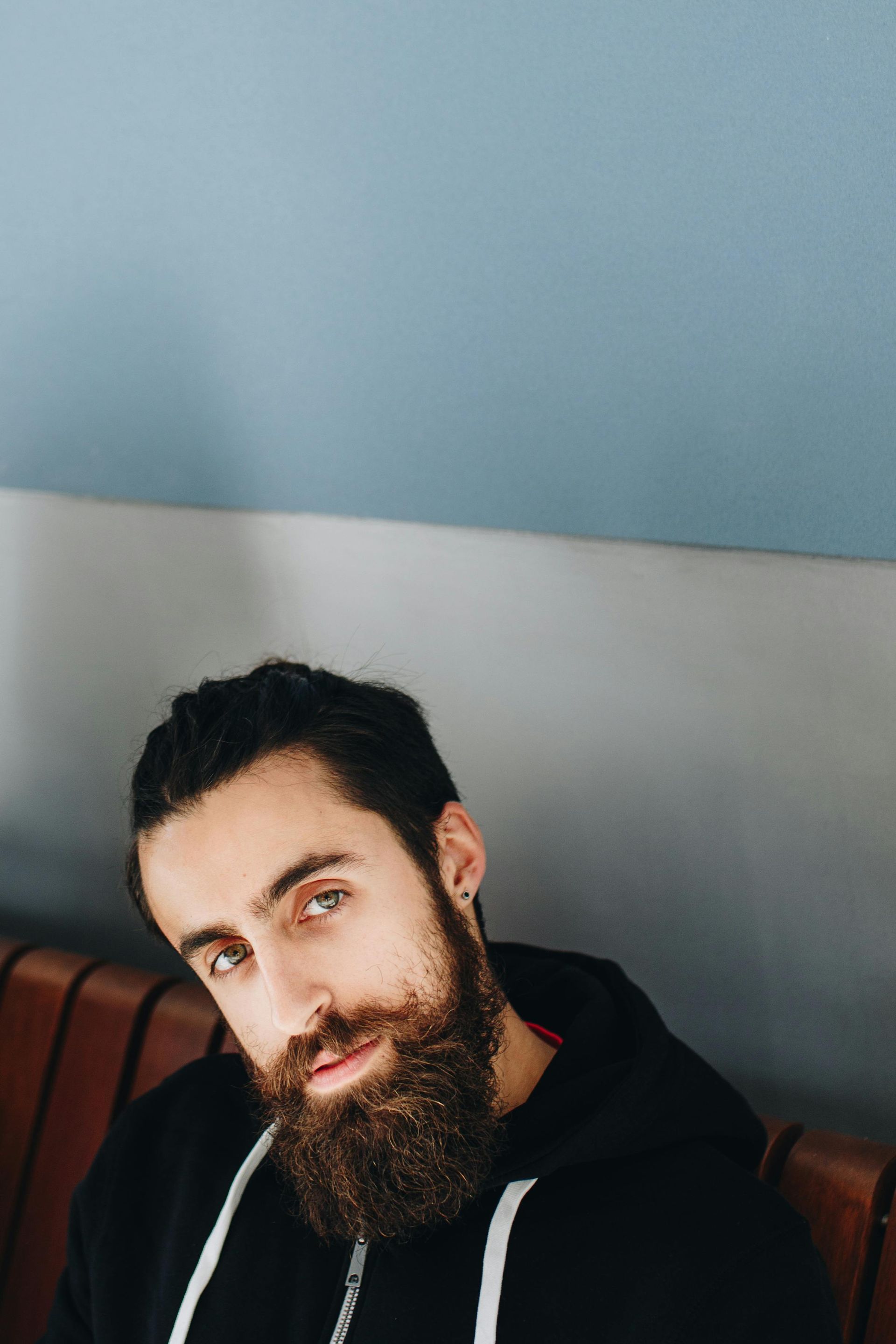 A man with a beard is sitting on a couch and looking at the camera.