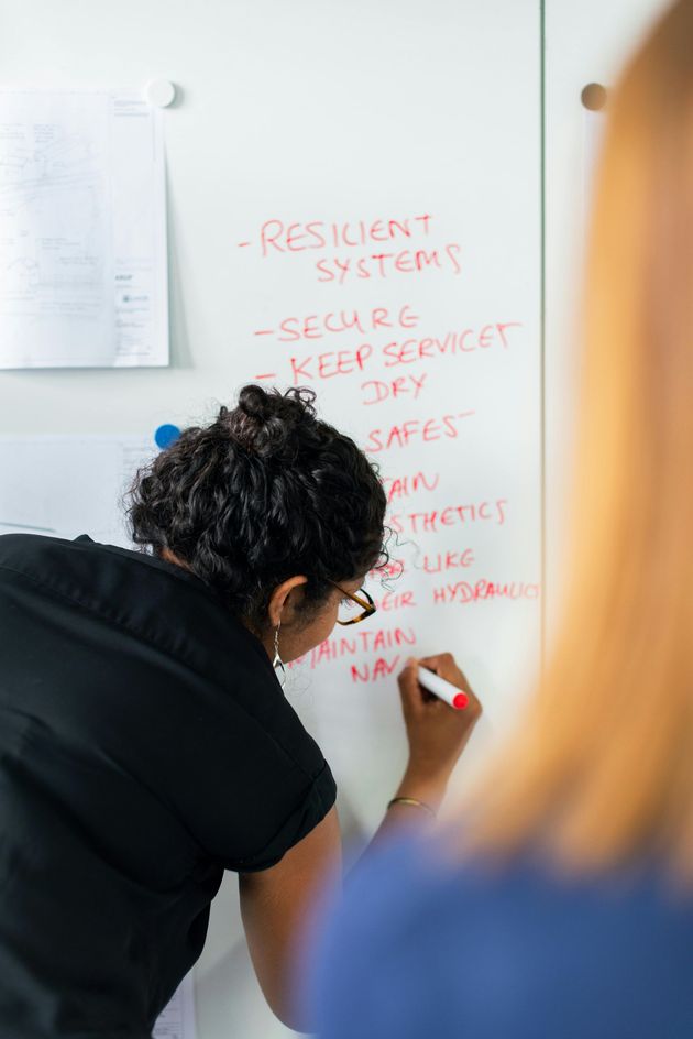 A woman is writing on a whiteboard with a marker.