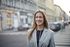 A woman in a suit is standing on a city street and smiling.