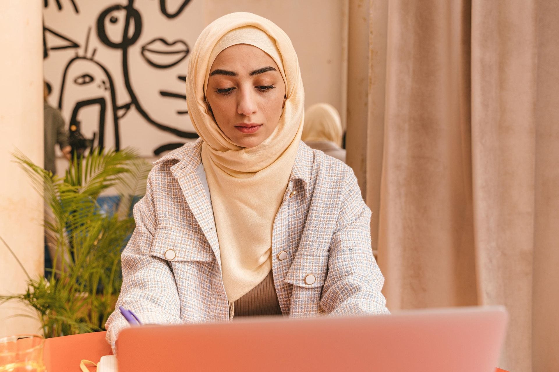 A woman in a hijab is sitting at a table using a laptop computer.