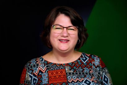 A woman wearing glasses and a colorful shirt is smiling for the camera.