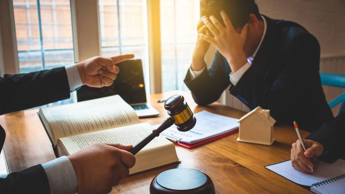 Lawyer points at stressed man, gavel and paperwork on table.