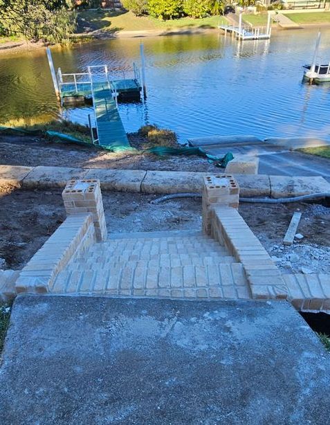 A Concrete Walkway Leading To A Lake With A Boat In The Water — Millers Masonry In Port Macquarie, NSW