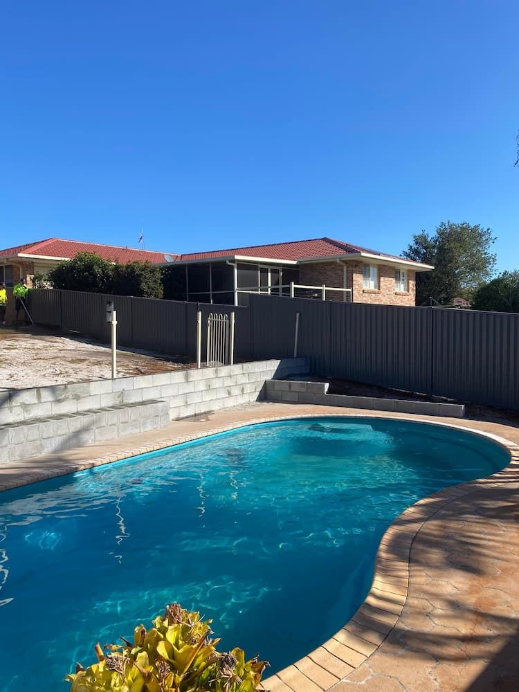 A Large Swimming Pool In Front Of A House With A Fence Around It — Millers Masonry In Kempsey, NSW