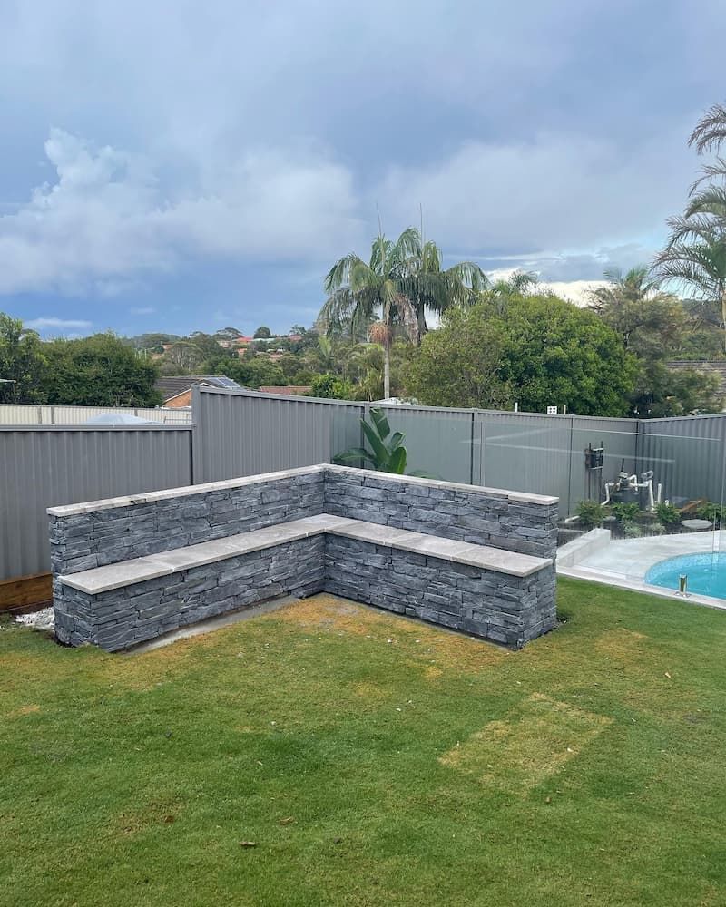 A Stone Bench Is Sitting In The Middle Of A Lush Green Yard — Millers Masonry In Wauchope, NSW