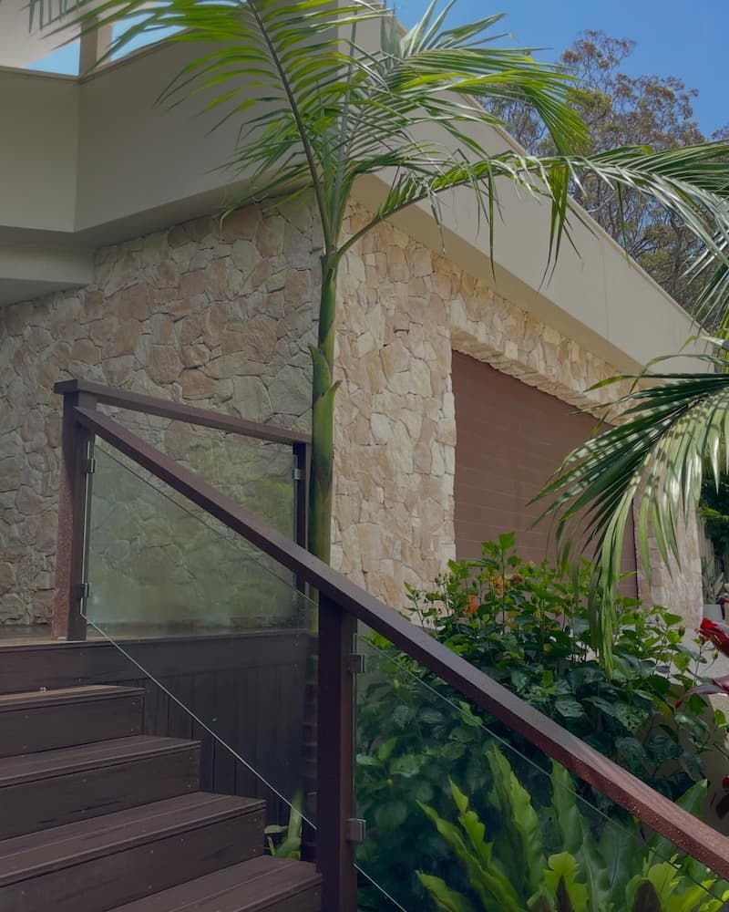A Staircase With A Glass Railing And A Palm Tree In The Background — Millers Masonry In Port Macquarie, NSW