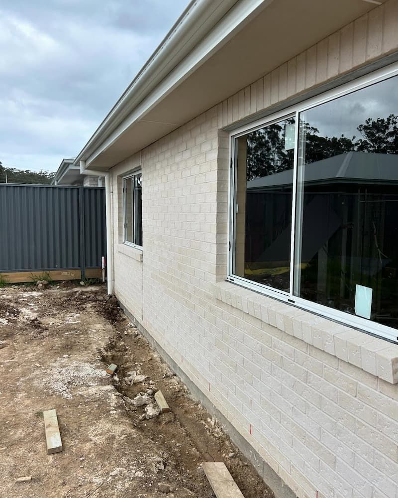 A White Brick House With Two Windows And A Fence — Millers Masonry In Laurieton, NSW