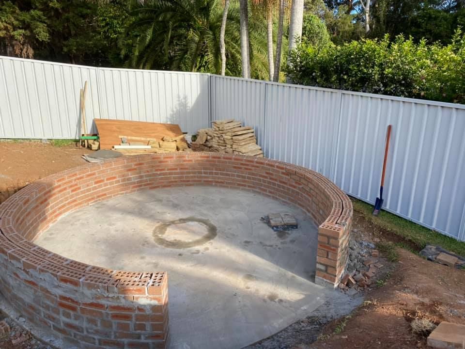 A Brick Circle Is Being Built In A Backyard Next To A White Fence — Millers Masonry In Port Macquarie, NSW
