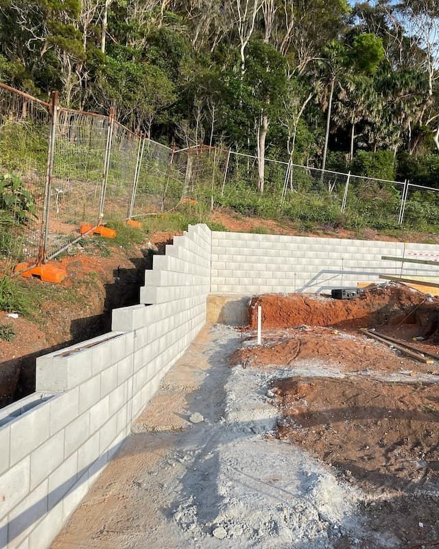 A Brick Wall Is Being Built In The Middle Of A Dirt Field — Millers Masonry In Port Macquarie, NSW