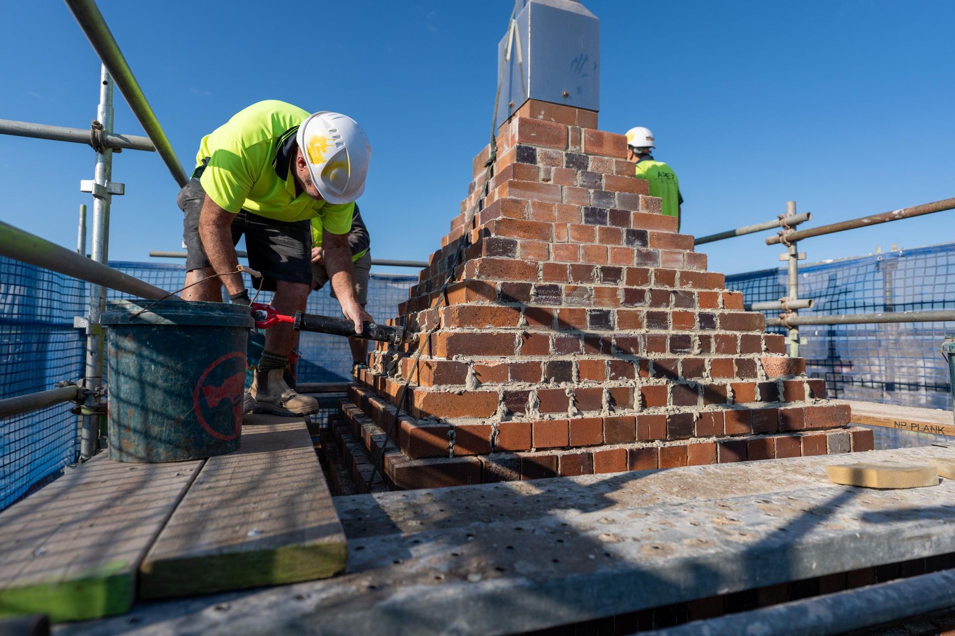 Bricklayer on Scaffolding, Building a Chimney with Red Bricks — Millers Masonry In Port Macquarie, NSW