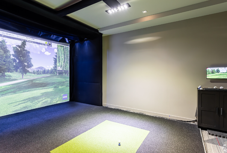 A golf simulator with a green mat and a large screen.