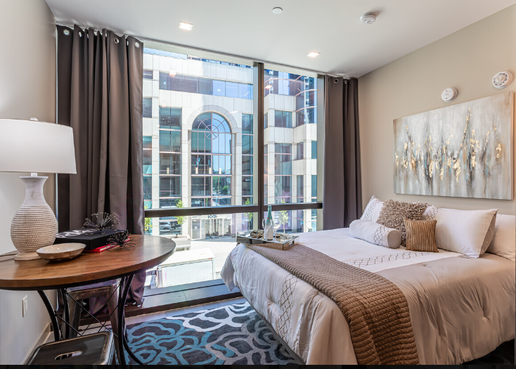 A bedroom with a large bed , a table , a lamp and a large window.