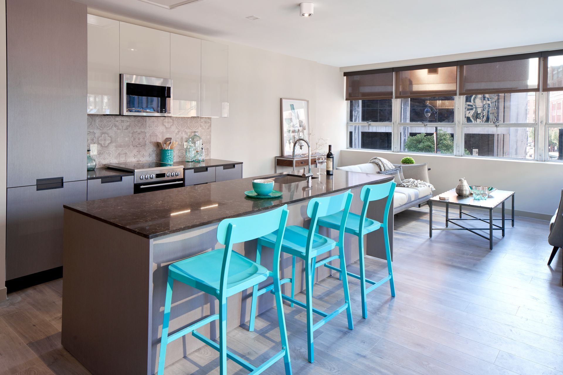 A kitchen with a large island and blue stools in a living room.