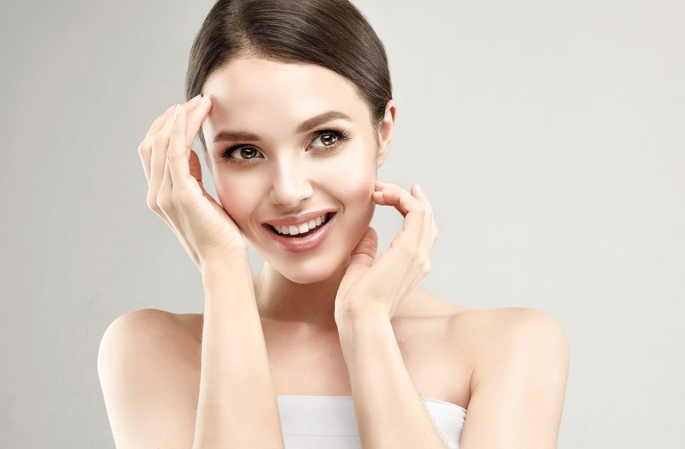A Woman is Smiling and Touching her Face with her Hands — Bersantai Medispa in Toukley, NSW