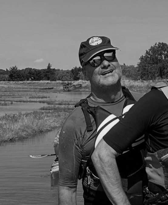 Man smiling, wearing a black and white life vest, natural outdoor background.