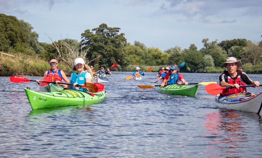 Kayakers paddling on a calm river. Green and white kayaks with colorful paddles under a sunny sky.