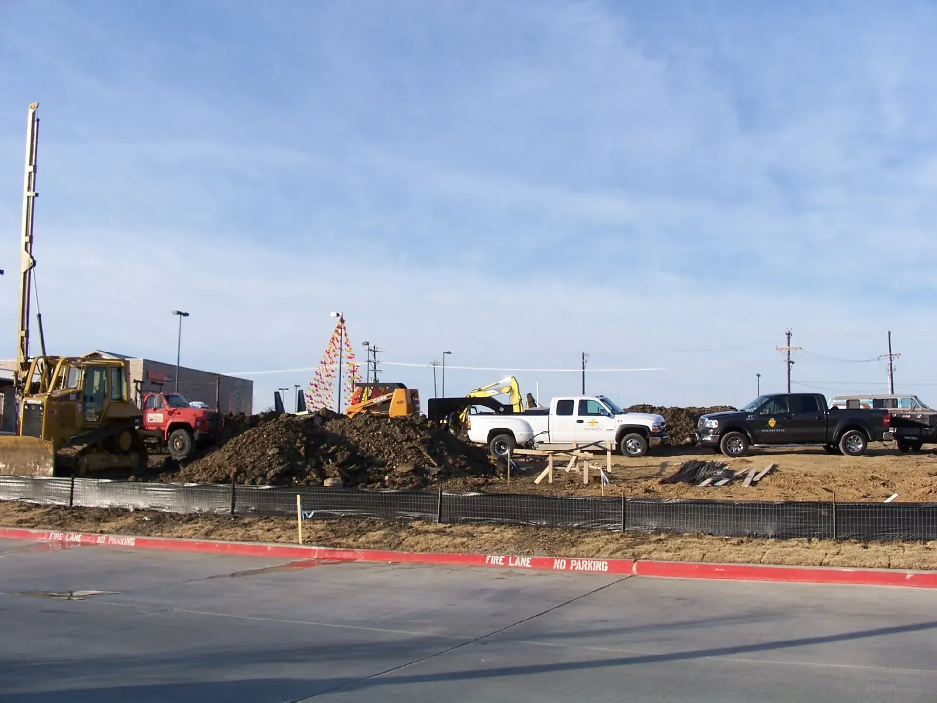 Construction site with heavy machinery: bulldozer, dump trucks, and a pile of dirt under a blue sky.