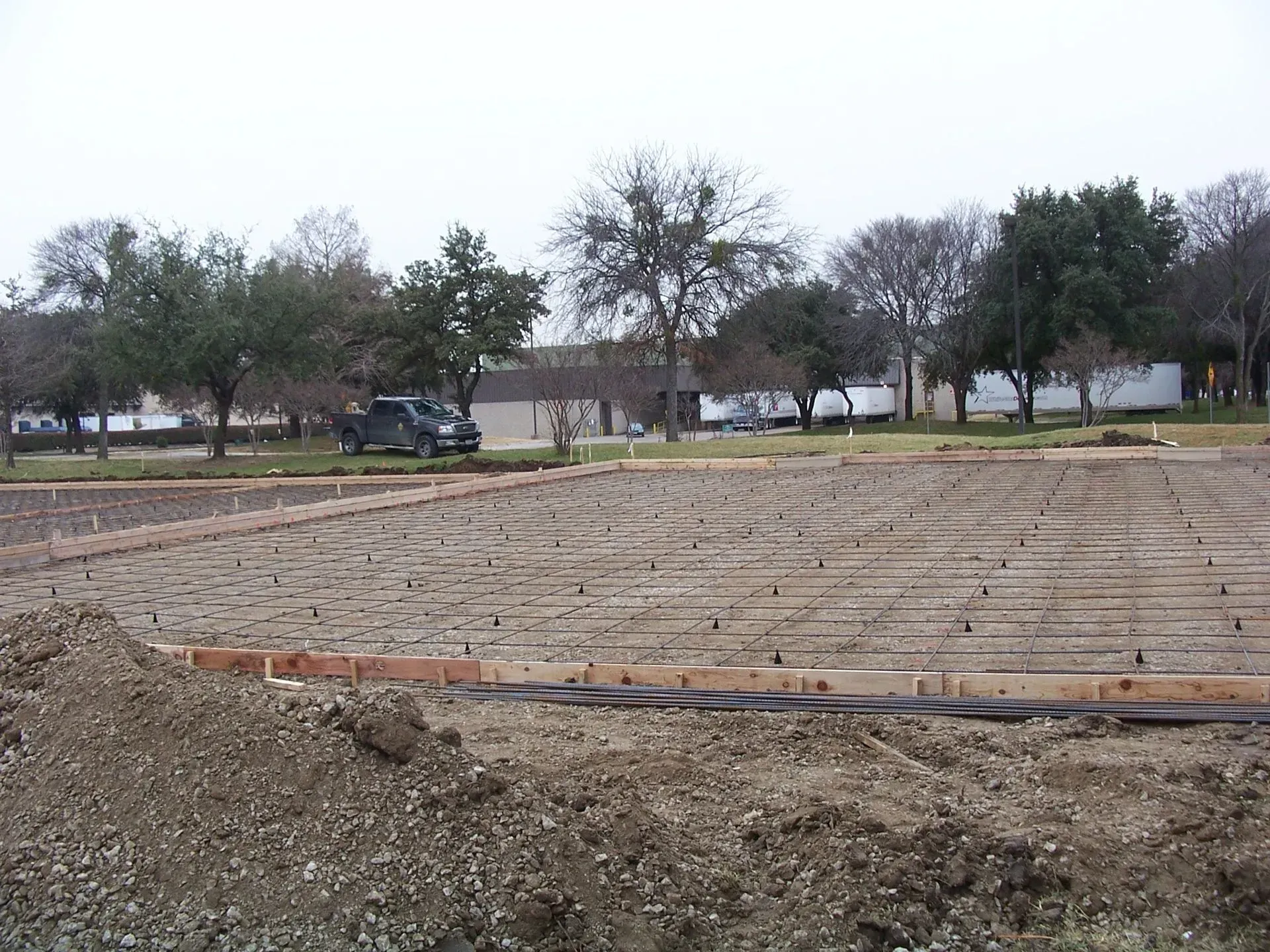 Construction site with exposed rebar grid, dirt, and surrounding trees.