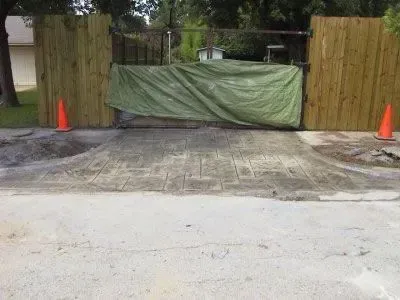 A driveway blocked by a green tarp and wooden fence sections, with orange traffic cones on either side.