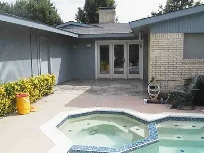 Pool and patio area with a hot tub, facing the exterior of a house with double doors.