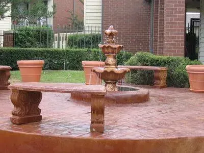 A tiered water fountain with stone benches and terracotta pots in a brick-paved courtyard.