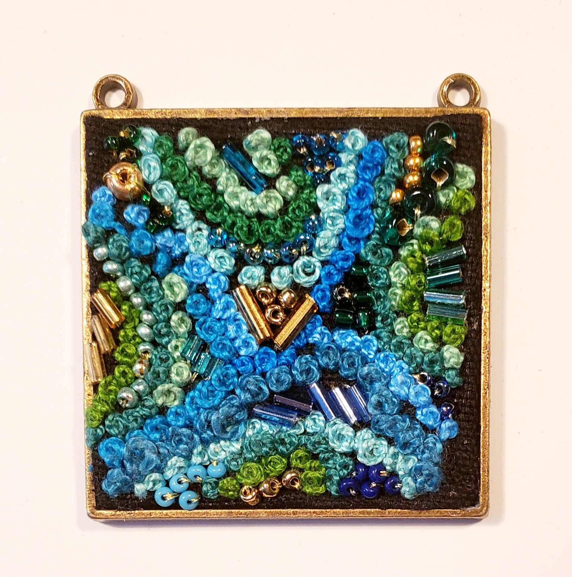 A square pendant with blue and green beads on it