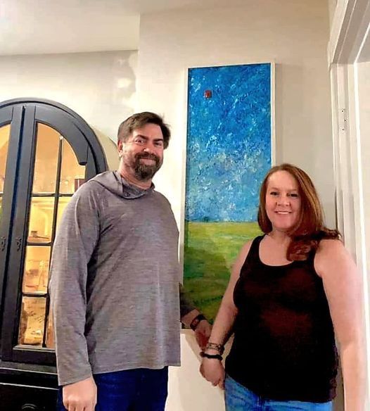 A man and a woman are standing next to each other in front of a painting.