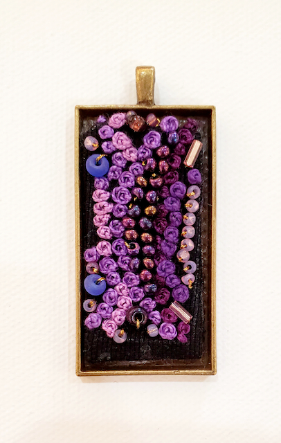 A pendant with purple beads in a gold frame on a white background.