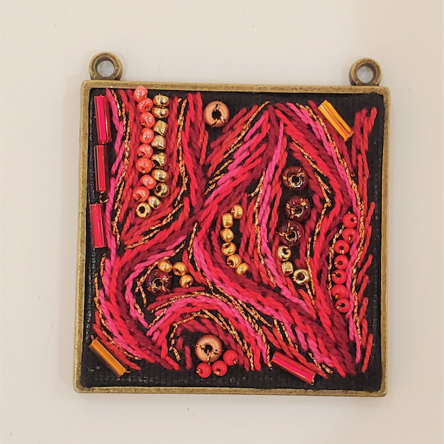 A square pendant with red and gold beads on it