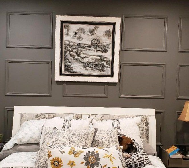 A bedroom with a bed , pillows , a lamp and a painting on the wall.