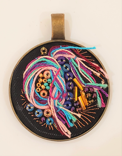 A round pendant with yarn and beads on it