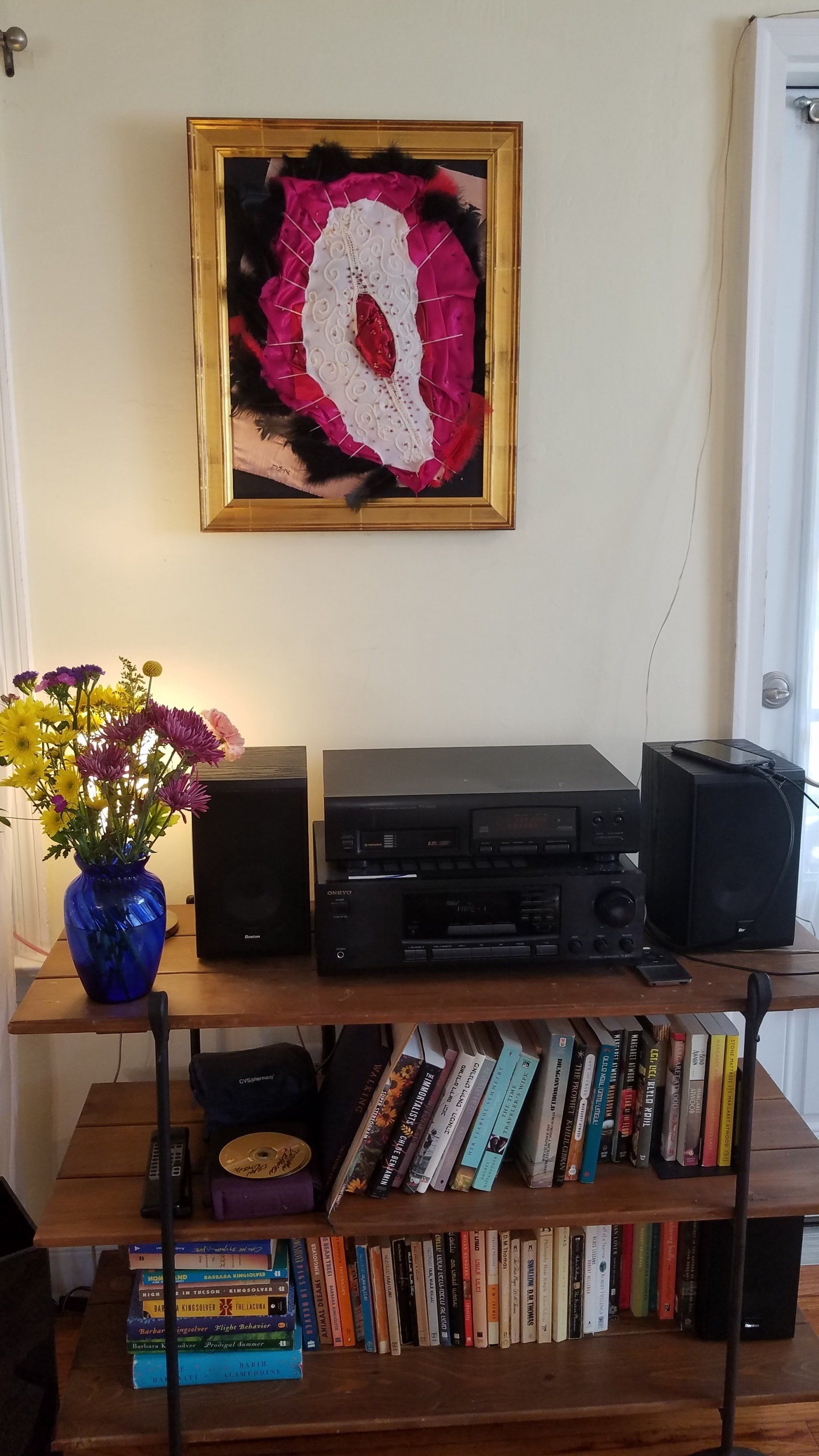 A living room with a shelf filled with books and a painting on the wall above it.